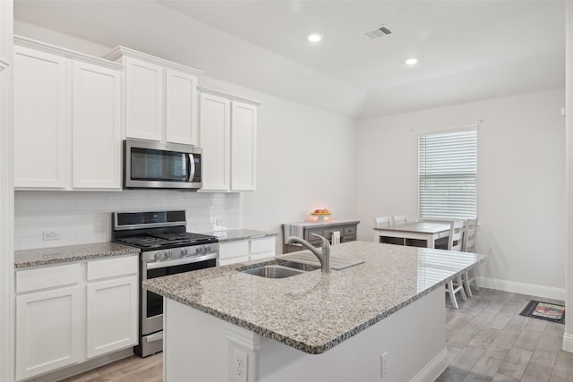 kitchen with stainless steel appliances, tasteful backsplash, light wood-style floors, white cabinets, and a sink