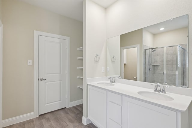 bathroom with double vanity, wood finished floors, a sink, and a shower stall