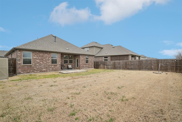 rear view of property with brick siding, a shingled roof, a lawn, a patio area, and a fenced backyard