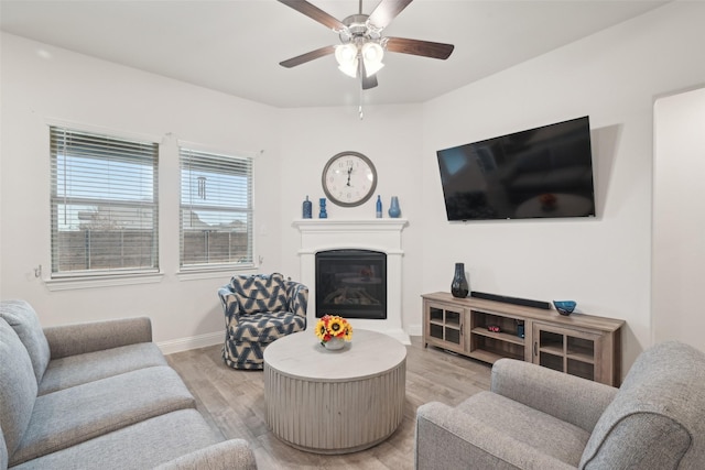 living area with light wood-style floors, a glass covered fireplace, ceiling fan, and baseboards