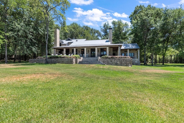 rear view of property featuring a standing seam roof, a chimney, metal roof, and a yard