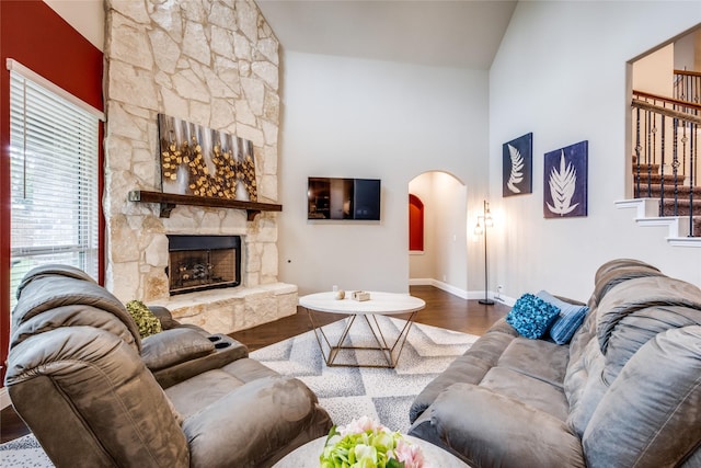 living area with arched walkways, a fireplace, stairway, wood finished floors, and baseboards