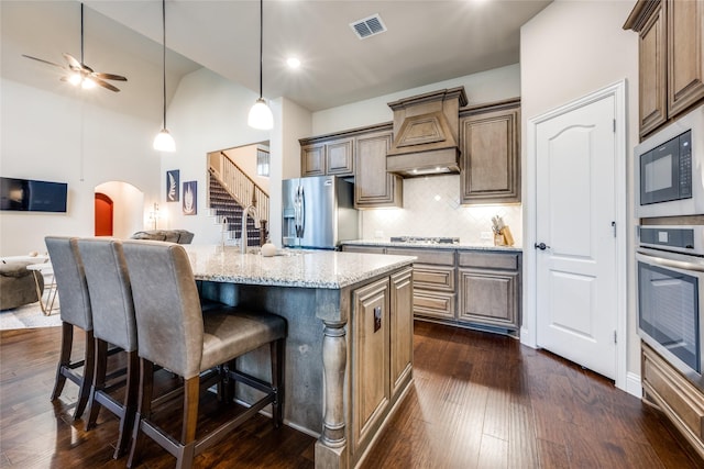 kitchen featuring arched walkways, stainless steel appliances, visible vents, custom range hood, and open floor plan