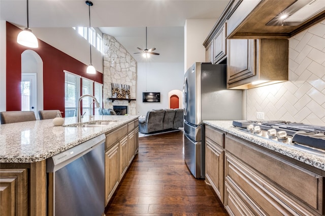 kitchen with arched walkways, appliances with stainless steel finishes, open floor plan, a sink, and wall chimney range hood