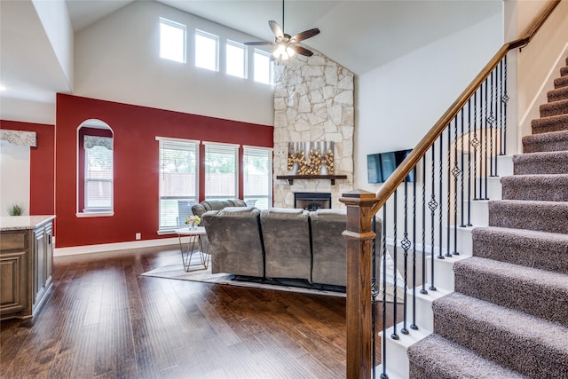 living room featuring dark wood-type flooring, a healthy amount of sunlight, ceiling fan, and a stone fireplace