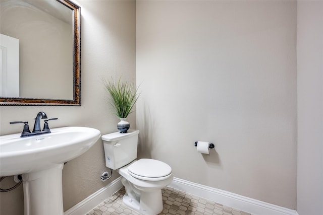 half bath with a sink, tile patterned floors, toilet, and baseboards