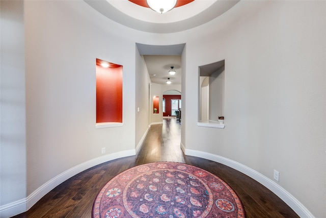 corridor with arched walkways, baseboards, and hardwood / wood-style floors