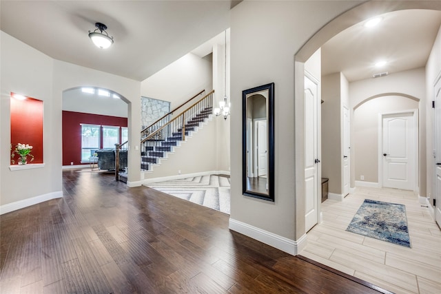 entrance foyer featuring light wood-type flooring, arched walkways, visible vents, and stairway