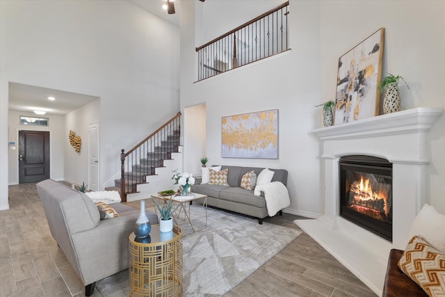 living area featuring baseboards, a glass covered fireplace, wood finished floors, a high ceiling, and stairs