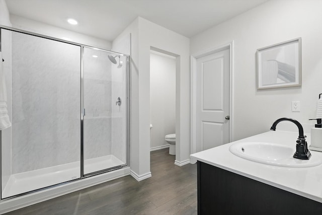 bathroom with toilet, wood finished floors, vanity, baseboards, and a shower stall