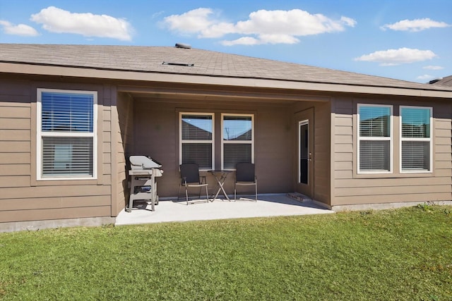 back of property with roof with shingles, a lawn, and a patio