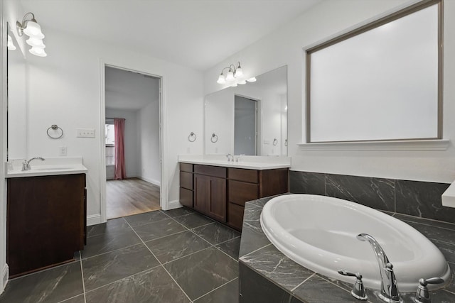 bathroom featuring a sink, two vanities, a bath, and baseboards