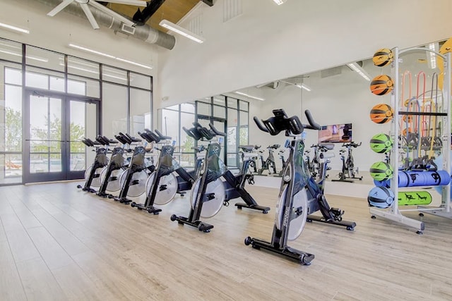 exercise room featuring a towering ceiling, french doors, wood finished floors, and a wealth of natural light