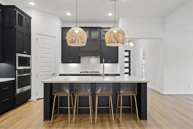 kitchen featuring light countertops, appliances with stainless steel finishes, light wood-style flooring, and a kitchen breakfast bar