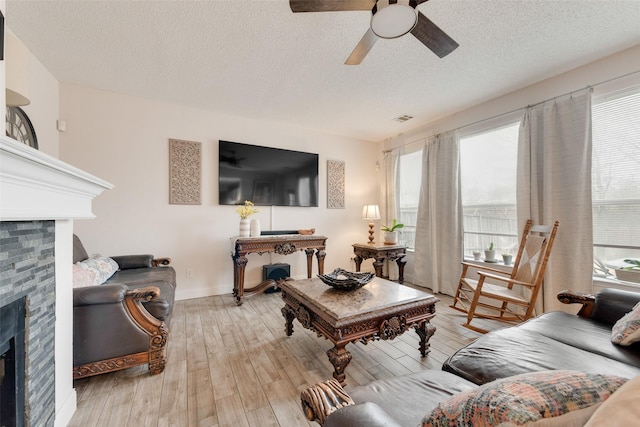 living area with a textured ceiling, a ceiling fan, baseboards, light wood-style floors, and a glass covered fireplace