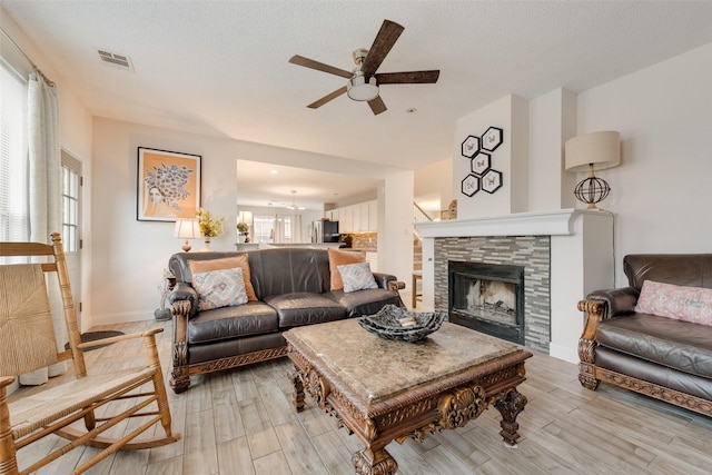 living area featuring light wood-style flooring, visible vents, a textured ceiling, and a stone fireplace