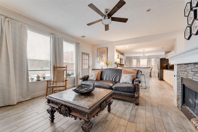 living area featuring plenty of natural light, a textured ceiling, light wood-type flooring, and a glass covered fireplace