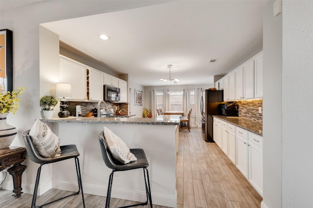 kitchen featuring stainless steel appliances, a peninsula, white cabinets, and light wood-style floors