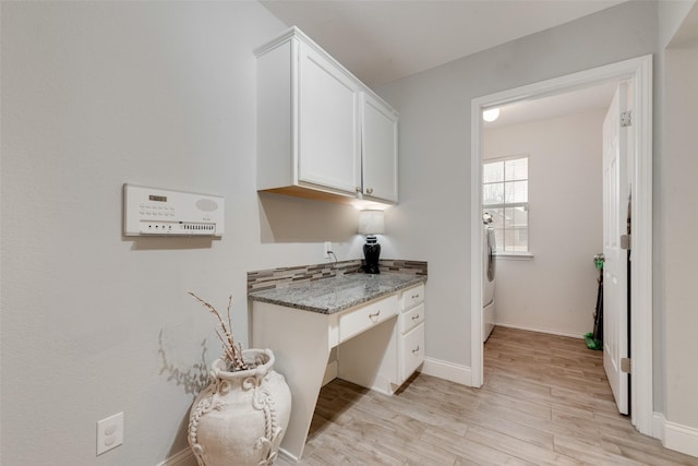 kitchen with washer / clothes dryer, light wood-style flooring, stone countertops, white cabinetry, and baseboards