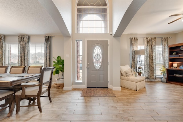 foyer entrance featuring arched walkways, a textured ceiling, a ceiling fan, baseboards, and light wood-type flooring