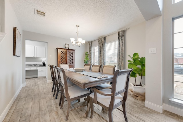 dining space featuring a chandelier, a textured ceiling, visible vents, baseboards, and light wood-type flooring