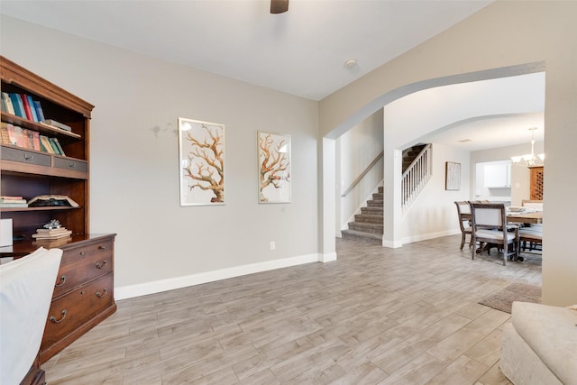 interior space featuring arched walkways, a notable chandelier, baseboards, stairs, and light wood finished floors