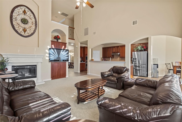 living room featuring light colored carpet, visible vents, a glass covered fireplace, and arched walkways