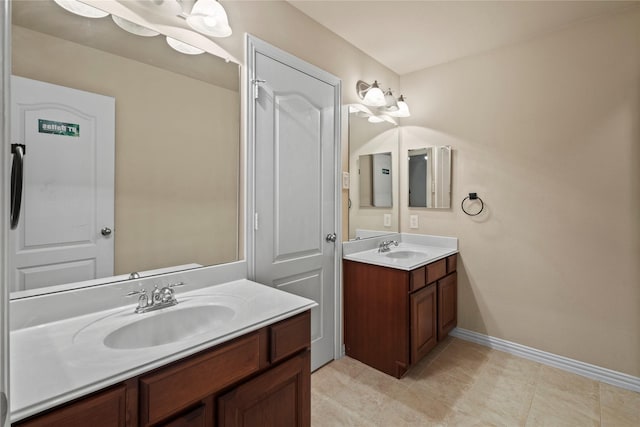 full bath with two vanities, a sink, and baseboards