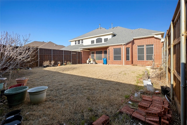 rear view of property with brick siding, a lawn, a fenced backyard, and roof with shingles