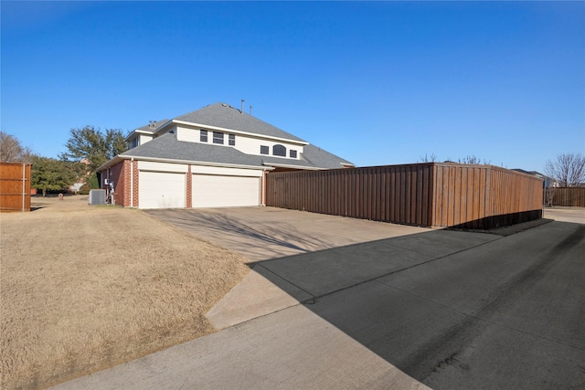 view of side of property with a garage, concrete driveway, fence, central air condition unit, and brick siding