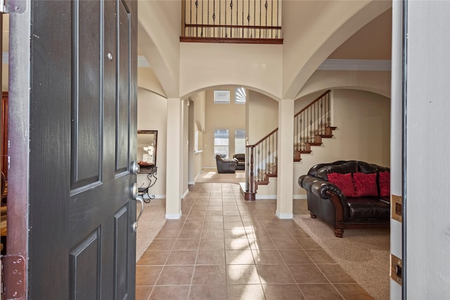 carpeted foyer entrance with stairs, a high ceiling, baseboards, and tile patterned floors