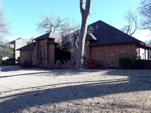 rear view of property featuring brick siding and roof with shingles