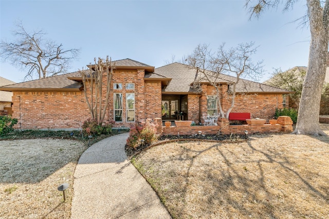 view of front of home featuring a patio area, roof with shingles, and brick siding