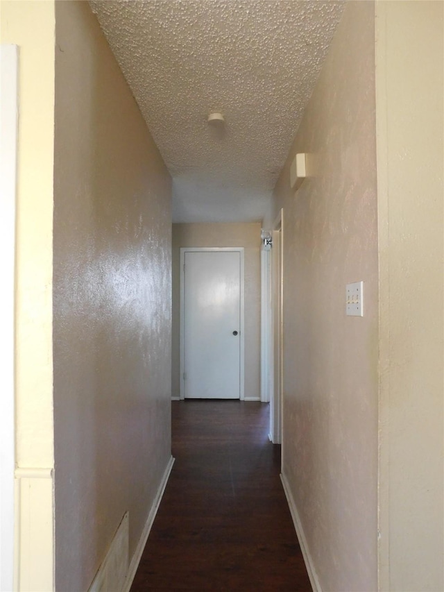 hallway featuring dark wood-style floors, a textured ceiling, and baseboards