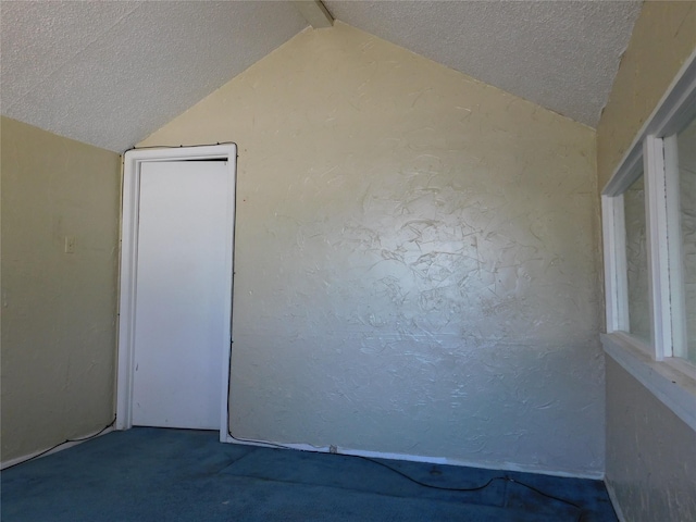 carpeted empty room featuring a textured wall, vaulted ceiling, and a textured ceiling