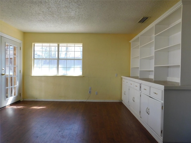 empty room with visible vents, dark wood finished floors, a textured ceiling, and baseboards