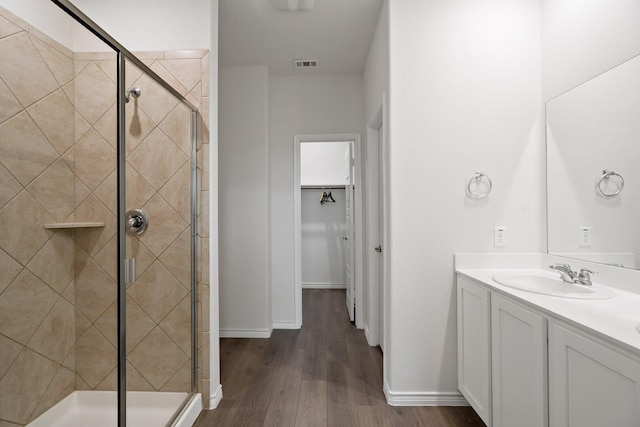 full bath with a stall shower, a spacious closet, visible vents, and wood finished floors