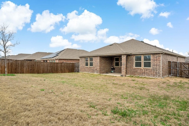 back of property with a shingled roof, a patio, a fenced backyard, a yard, and brick siding