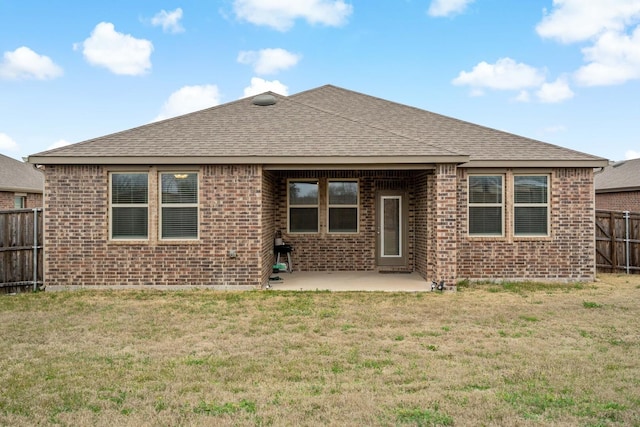 rear view of property with a shingled roof, a patio, fence, a yard, and brick siding