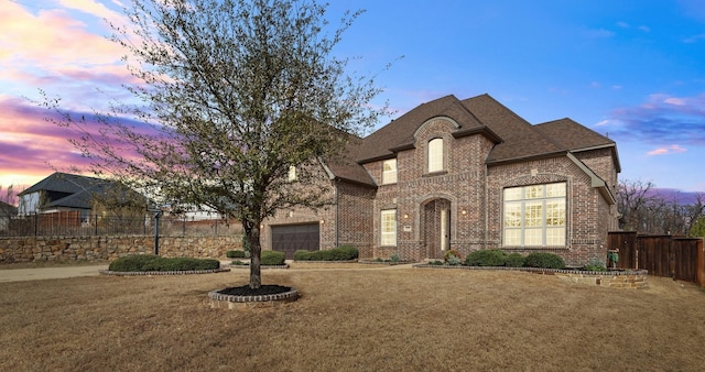 french country inspired facade with a garage, brick siding, fence, and a lawn