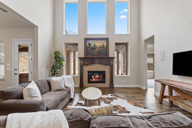 living room featuring visible vents, baseboards, wood finished floors, a high ceiling, and a fireplace