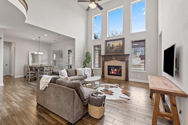 living room with recessed lighting, a glass covered fireplace, wood finished floors, baseboards, and ceiling fan with notable chandelier