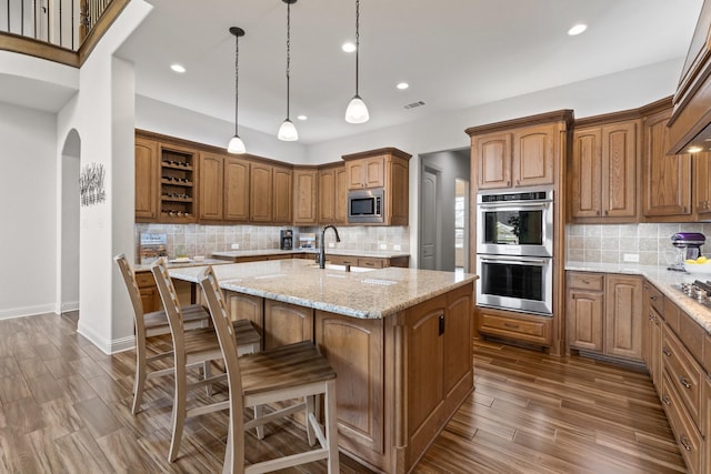 kitchen featuring visible vents, appliances with stainless steel finishes, light stone countertops, open shelves, and an island with sink