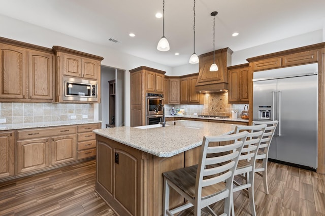 kitchen featuring built in appliances, dark wood-type flooring, visible vents, an island with sink, and custom range hood