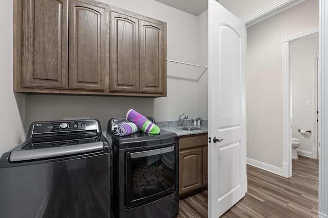 laundry room with wood finished floors, a sink, baseboards, washer and dryer, and cabinet space