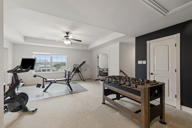 workout room with a ceiling fan, a tray ceiling, light carpet, and baseboards