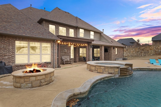 exterior space featuring a shingled roof, a patio area, brick siding, and a fire pit