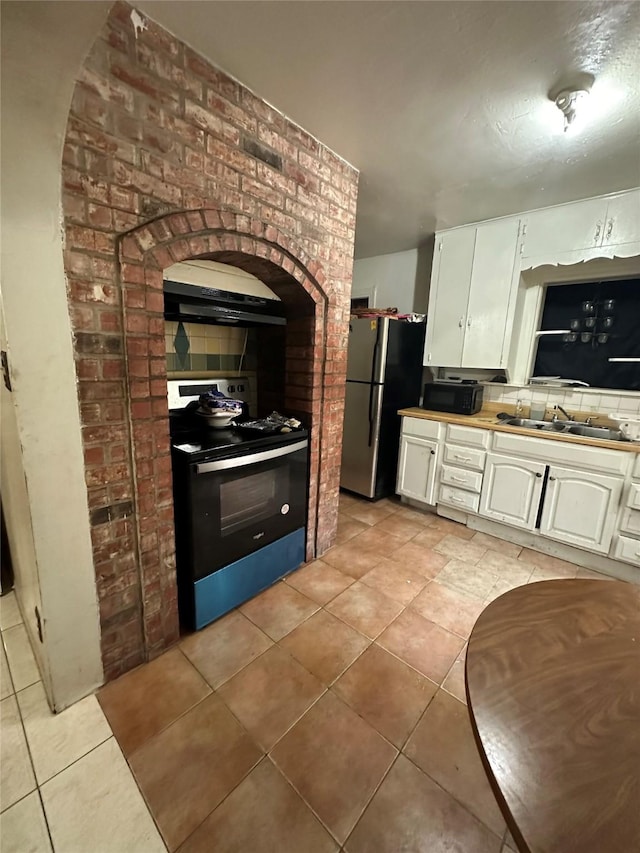 kitchen featuring light tile patterned floors, under cabinet range hood, a sink, freestanding refrigerator, and electric range oven