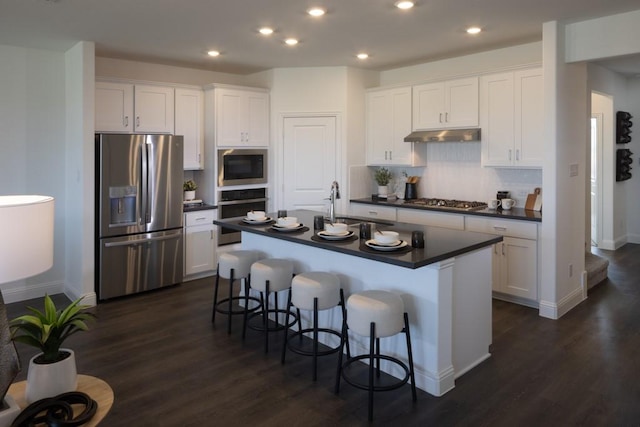 kitchen featuring a breakfast bar area, dark countertops, appliances with stainless steel finishes, white cabinets, and a sink