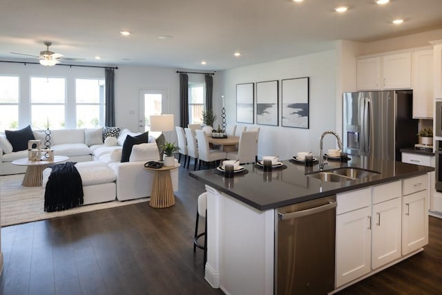 kitchen featuring open floor plan, stainless steel appliances, dark countertops, and a sink